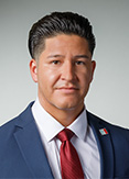 Marcus is wearing a blue blazer, white shirt, and red tie. 