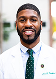 Raymond is wearing a white coat and green polka dot tie.