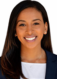 Falen Demsas has straight long black hair. She is wearing a white blouse and black jacket.