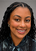 Tiana Walker has long braided black hair. She is wearing a dark patterned blouse.