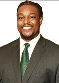 Matthew Moore is wearing a green patterned tie, white shirt, and gray jacket.
