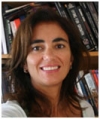  Arachu Castro is standing in front of a bookshelf filled with books. She has medium-length brown hair.