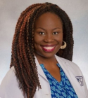 Carmen Tchokonthé Monthé-Drèze has long brownish black hair. She is wearing a blue patterned shirt and white coat.