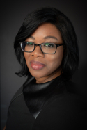 Davene Wright is wearing a black blouse. She has medium length black hair and glasses.