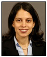  Lucia Sobrin is wearing a black blazer, light gray shirt, and pearl necklace.