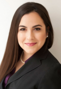 Monik Jimenez has long straight brown hair. She is wearing a necklace, black blazer, and purple blouse.