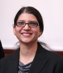 Sarosh Rana is wearing a black blazer and gray blouse. She has glasses and is wearing her hair in a ponytail.
