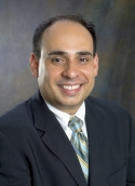 Arturo Saavedra is wearing a white shirt, black blazer, and green patterned tie.