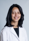 Elsie M. Taveras is wearing a white coat and black shirt. She has medium length black hair.