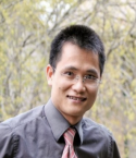 Bon Trinh is standing outside by some trees. He is wearing a gray shirt and red patterned tie.