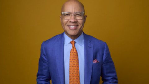 A waist-up photo of Darren Walker, smiling in a bright blue suit and orange tie. 