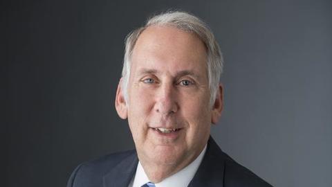 Edward Halperin is wearing a black blazer, white shirt, and blue striped tie.