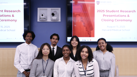 Seven Project Success student smile at the camera. They are standing in front of a screen that says, "2025 Student Research Presentations and Closing Ceremony."