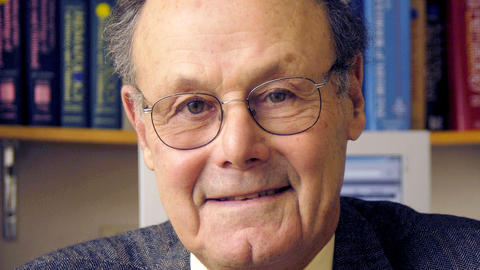 David Nathan sitting in front of a bookshelf. He is wearing a blue patterned blazer, yellow shirt, and red tie.