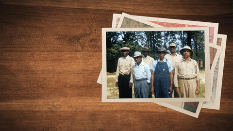 A photo of a group of Black men sits on a pile of more photos on a wooden surface.
