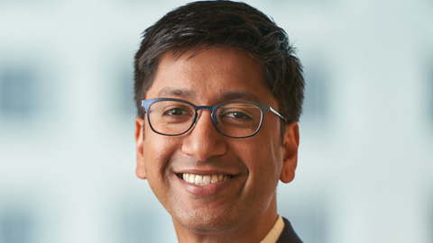 Guarav Singal is wearing a white shirt and black blazer. He has black-rimmed glasses and is smiling.
