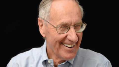 Frederick Lovejoy has short gray hair and glasses. He is wearing a light gray shirt and smiling towards the right.