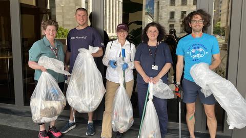 Michelle Keenan stands alongside four other volunteers outside the Kresge building. They are all holding clear trash bags filled with trash and four of the volunteers also have trash pickers.
