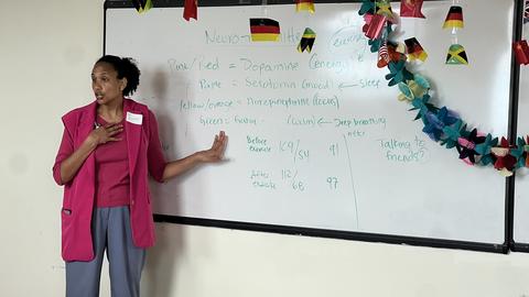 Frinny Polanco is gesturing to herself and a whiteboard with neurotransmitter terms on it.