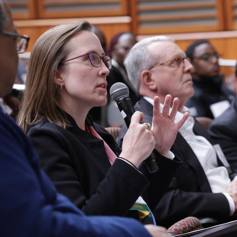 A women with blonde hair and glasses speaks into a microphone as she sits in a row in the Joseph B. Martin Conference Center in TMEC.