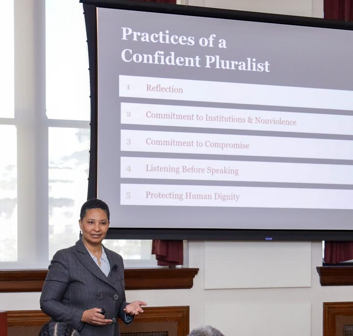 Danielle Allen stands in front of a projector screen with the 5 practices of pluralism on it. 