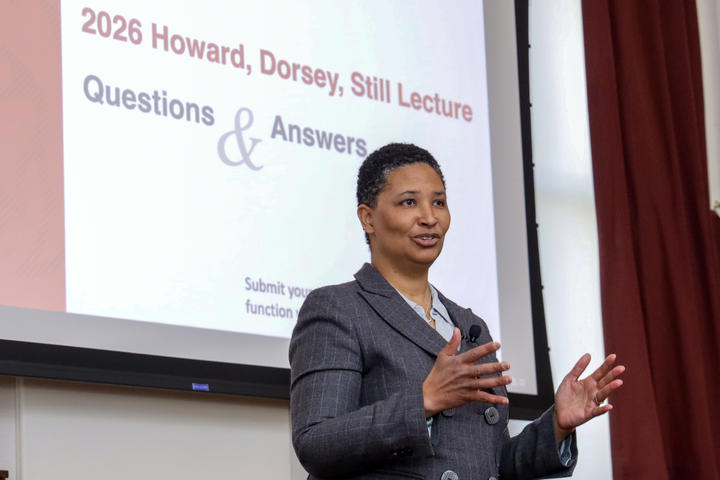 Danielle Allen stands in front of a projector screen in the Waterhouse Room. Both her hands are raised in gesture as she speaks.