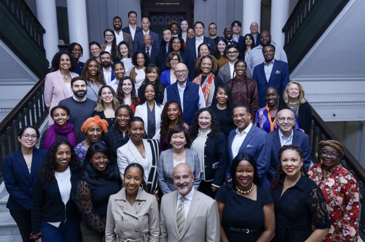 A group of Commonwealth Fund Fellowship alumni are standing on steps in the Waterhouse Room and smiling for a photo.