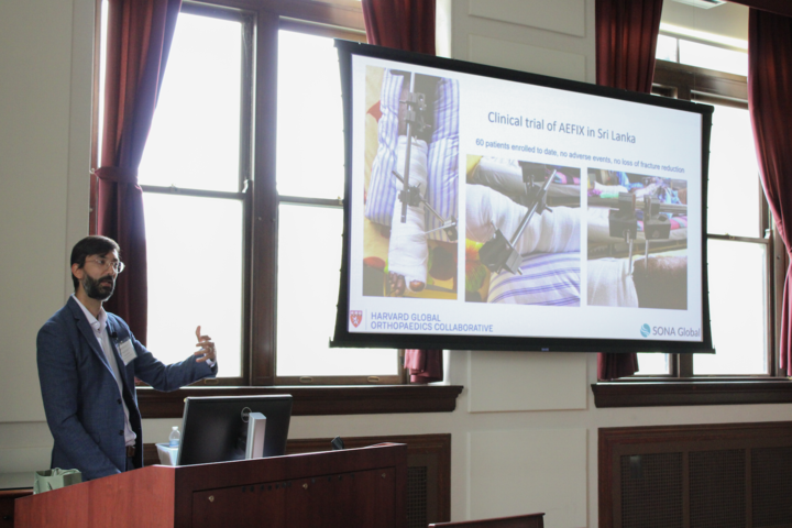 Kiran Agarwal-Harding stands behind a lectern as he gestures towards a projecter screen in the Waterhouse Room of Gordon Hall.