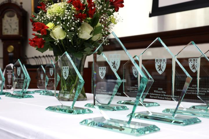 Angular crystal awards and a vase of flowers are on a white tablecloth-covered table.
