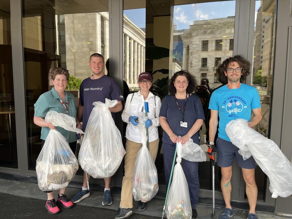 Michelle Keenan stands alongside four other volunteers outside the Kresge building. They are all holding clear trash bags filled with trash and four of the volunteers also have trash pickers.