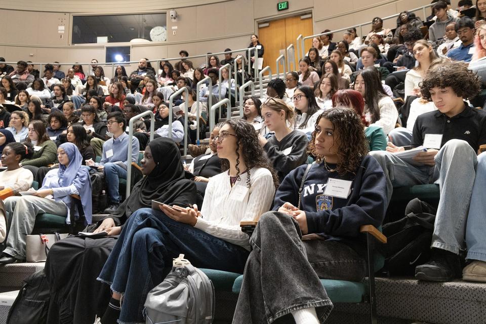 A large group of people sit in the amphitheatre in TMEC. 