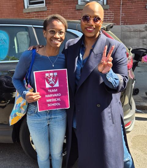 One of the Longwood Campus team members poses with a sign alongside MA Congresswoman Ayanna Pressley who is flashing a peace sign.