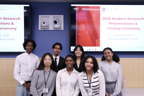 Seven Project Success student smile at the camera. They are standing in front of a screen that says, "2025 Student Research Presentations and Closing Ceremony."