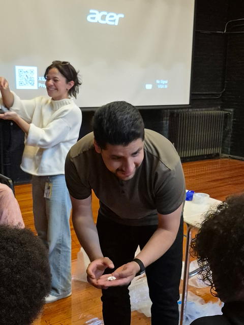 Ricky Silva and Christine Kalinski are standing in front of a projector and showing students pieces of candy.