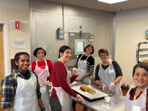 Six OCCE staff members standing around a metal table with a tray of food ready to be packed.