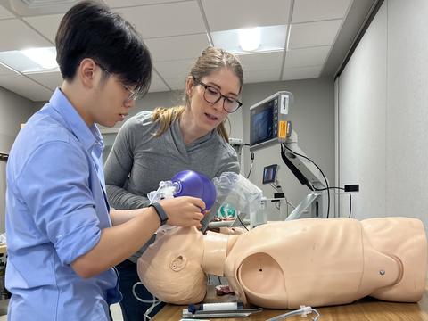 A Project Success student uses a bag valve mask on a dummy while a surgical resident monitors his technique.