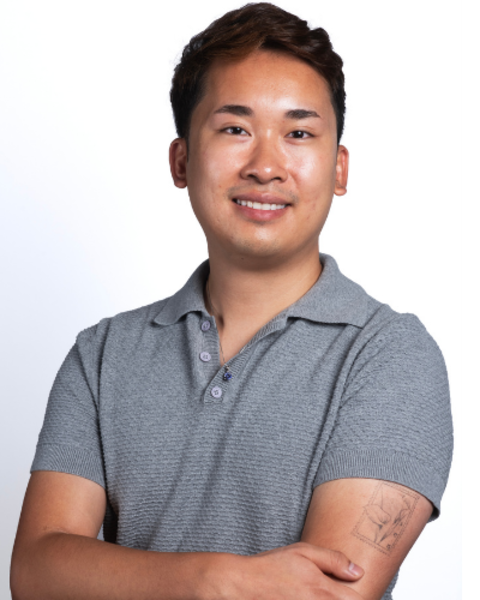 Rory Vu poses with his arms crossed. A fine line floral tattoo is visible on his upper left arm and he is wearing a ring on his right ring finger.