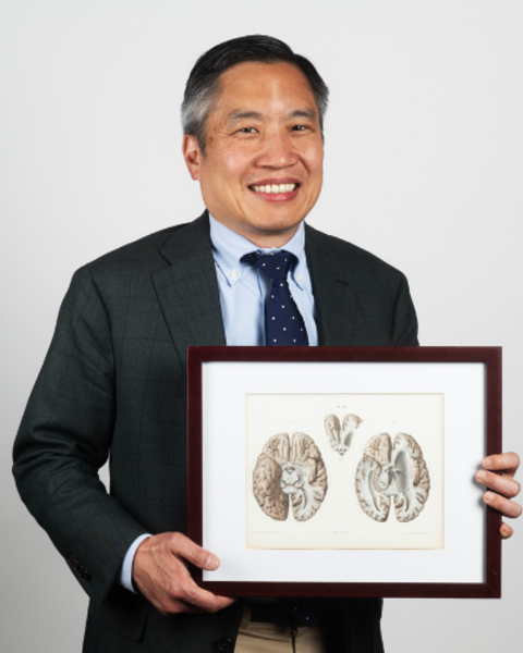 Bernard Chang is holding up a framed lithograph of a brain.