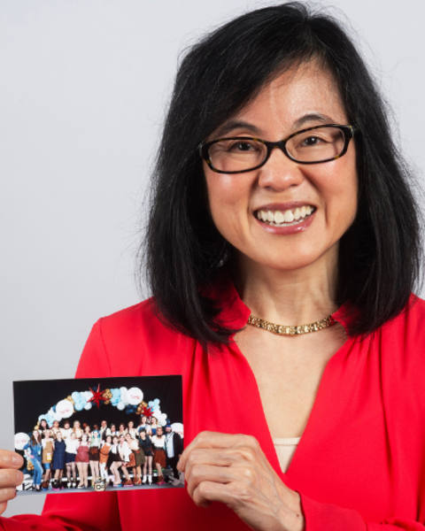 Grace Huang is holding a group photo of her skating team. She is wearing a red blouse.