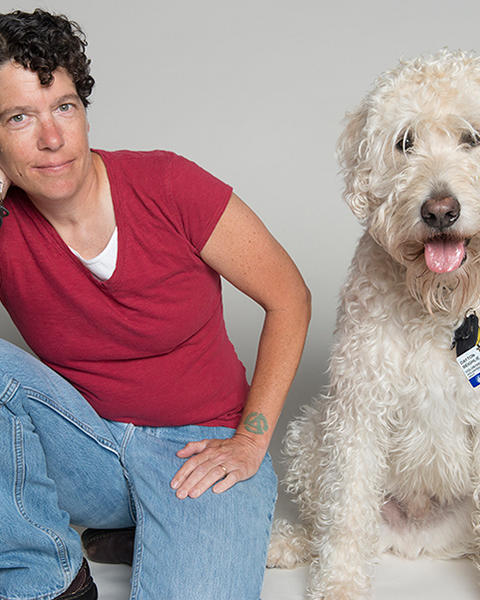 Beth Beighlie is kneeling on the ground with her dog Dayton beside her. He is a large white curly-haired dog who has his own Boston Children's Hospital ID.