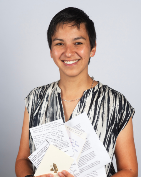 Tari Tan is wearing a black and white printed blouse. She is holding a bunch of cards and notes from students.