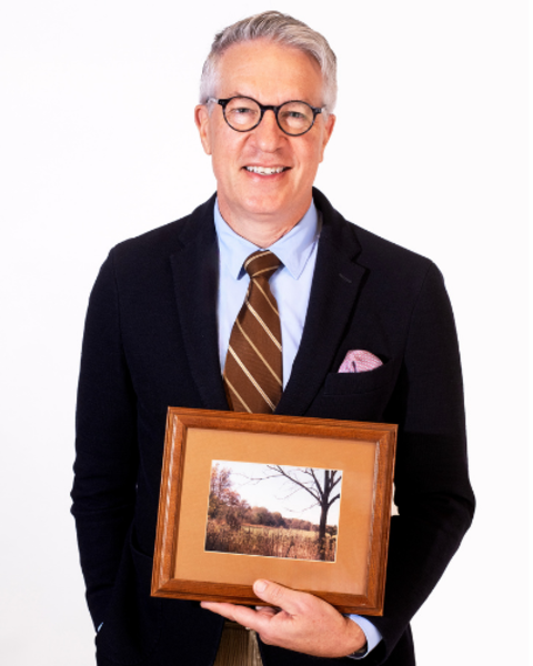 William Giannobile is holding a wooden framed photo of his family's farmland in Missouri. 