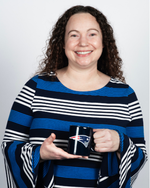 Lorien Hecht is wearing a horizontally striped blue, white, and black top. She is holding a Patriots mug.