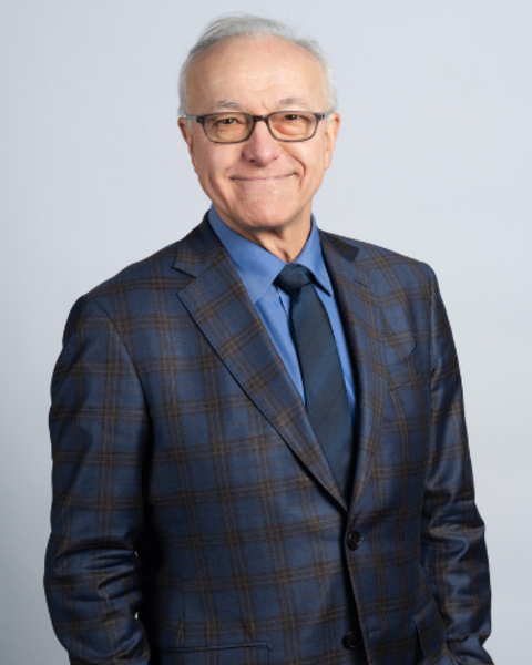 George Daley is wearing a plaid dark blue suit, blue shirt, and dark blue tie. He is casually standing with his hands in his pant pockets.