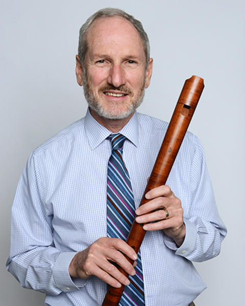 David Bor is holding a renaissance recorder which looks like a long wooden flute. 