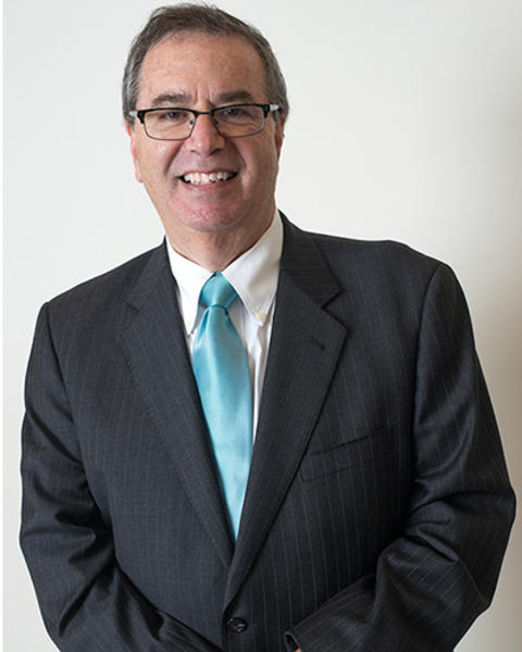 Jeffrey Flier is wearing a black striped blazer, white shirt, and turquoise tie. His hands are clasped in front of him.