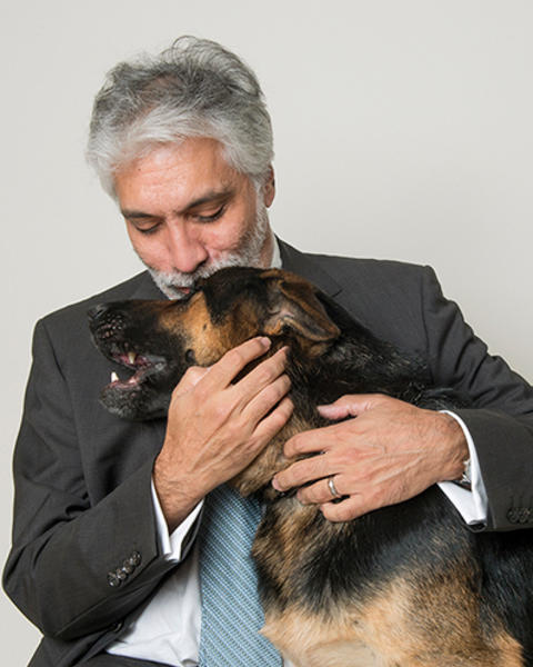 Sanjay Gulati is kissing his hearing dog, Plato, on the forehead. Plato's fur is black and brown.