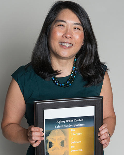 Sharon Inouye is holding a framed flyer of the 2006 Aging Brain Center Scientific Symposium.