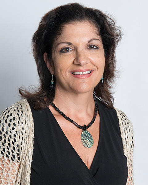 Christina Ferlisi Kennedy is wearing a mesh beige cardigan, black blouse, and necklace with a shiny flat pendant.