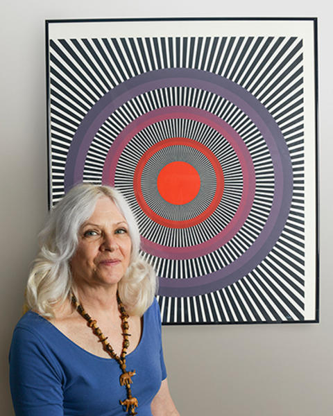 Margaret Livingstone sits in front of an Isia Leviant print, which is comprised of purple and red circles and black and white radiating lines.
